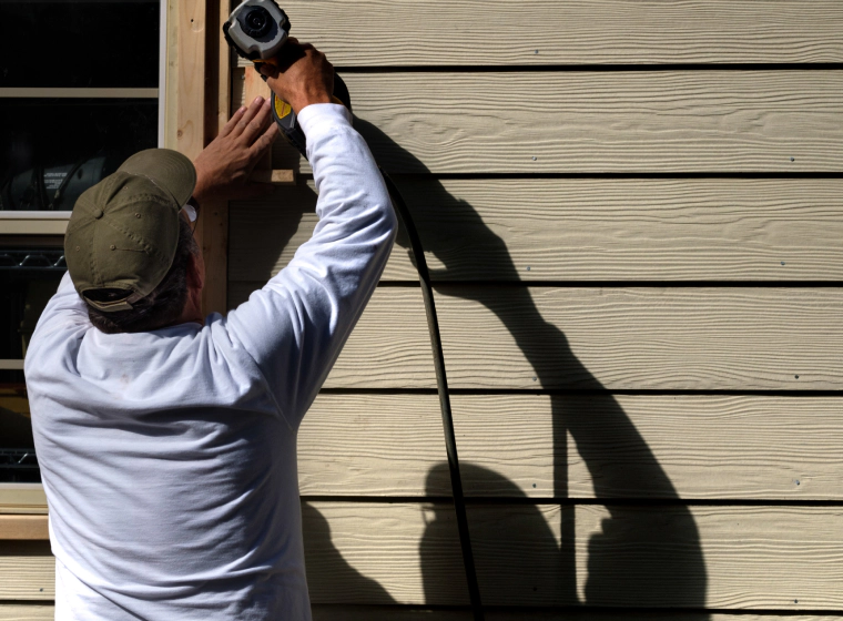 contractor installing the beige siding of a house